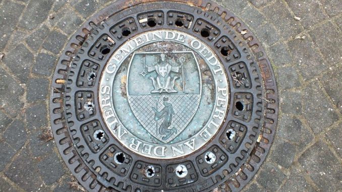 Der einzige Kanaldeckel mit dem Wappen der alten Gemeinde Oedt liegt neben der Skulpturengruppe "Bauer und Weber" am Niedertor in Oedt. (foto/mb)