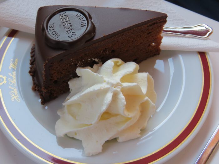 Ein Stück Sachertorte auf einem Teller mit einem Klecks Sahne daneben.