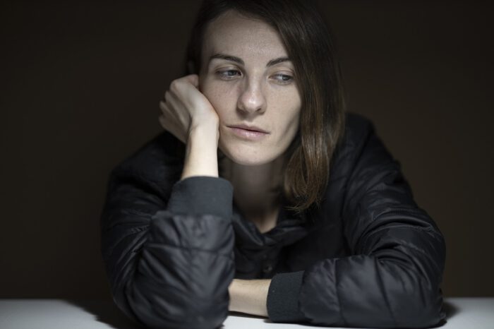 Eine nachdenkliche Frau mit kurzer Frisur, die auf ihren Händen stützt und in die Ferne blickt.