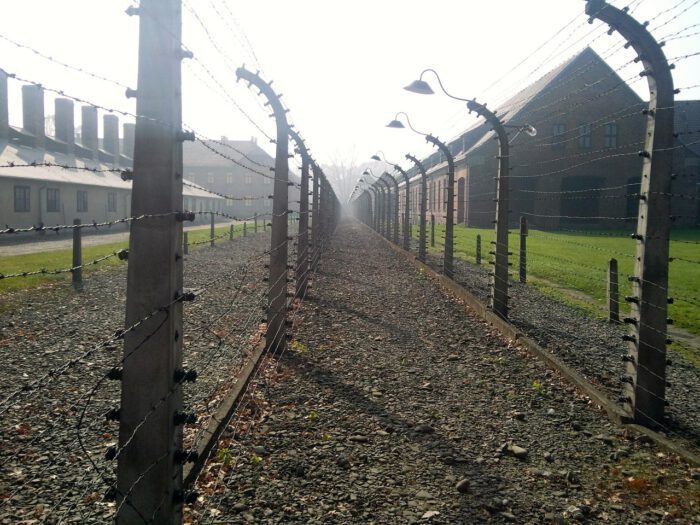 Stacheldrahtzaun entlang eines Weges in einem ehemaligen Konzentrationslager, umgeben von Nebel.