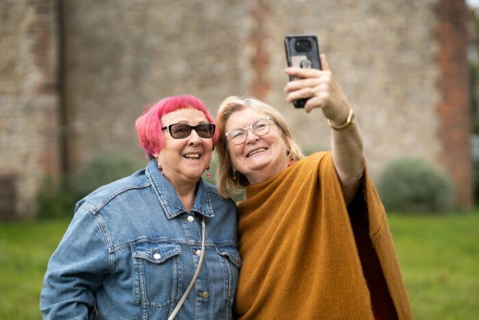 Two smiling senior women take a selfie outdoors captured in a candid moment.