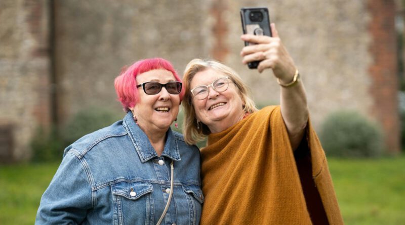 Two smiling senior women take a selfie outdoors captured in a candid moment.