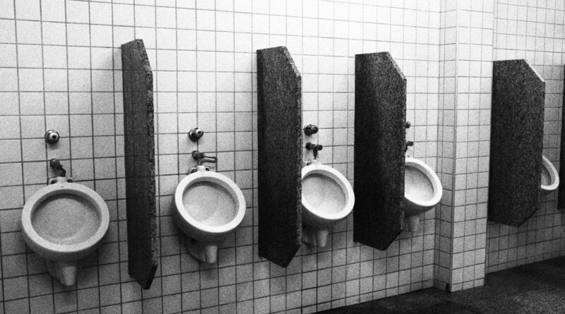 Urinals in a bathroom, separated by wood.
