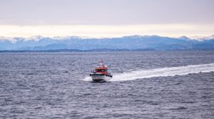 A speedboat traveling across the open sea with scenic snow-capped mountains in the background.