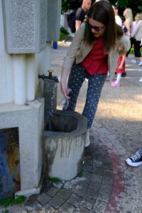 A woman fills a glass from an outdoor stone fountain.