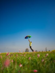 Person with rainbow umbrella standing in a vibrant meadow under a clear summer sky.