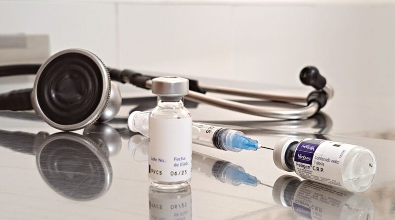 Close-up of vaccines, syringe, and stethoscope on a reflective surface in a clinical setting.