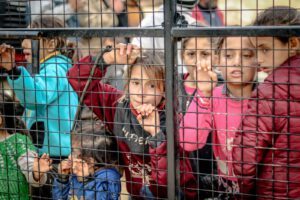 A poignant image of children behind a metal fence in Idlib, Syria, highlighting togetherness and diversity.
